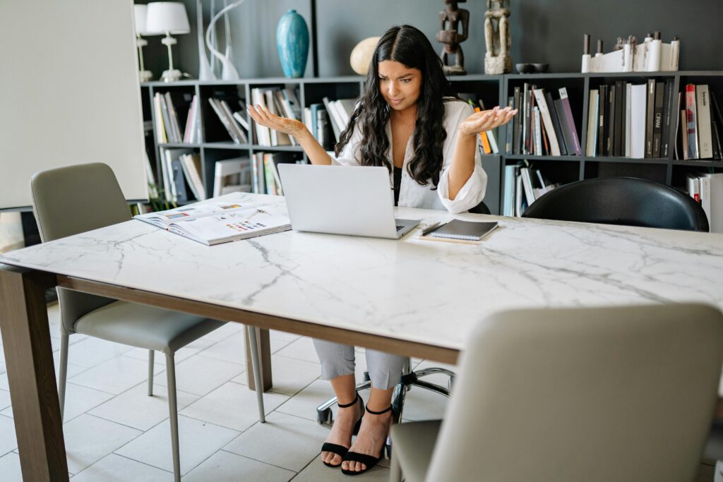 Woman sitting in an office with a laptop, working remotely with a confused expression.